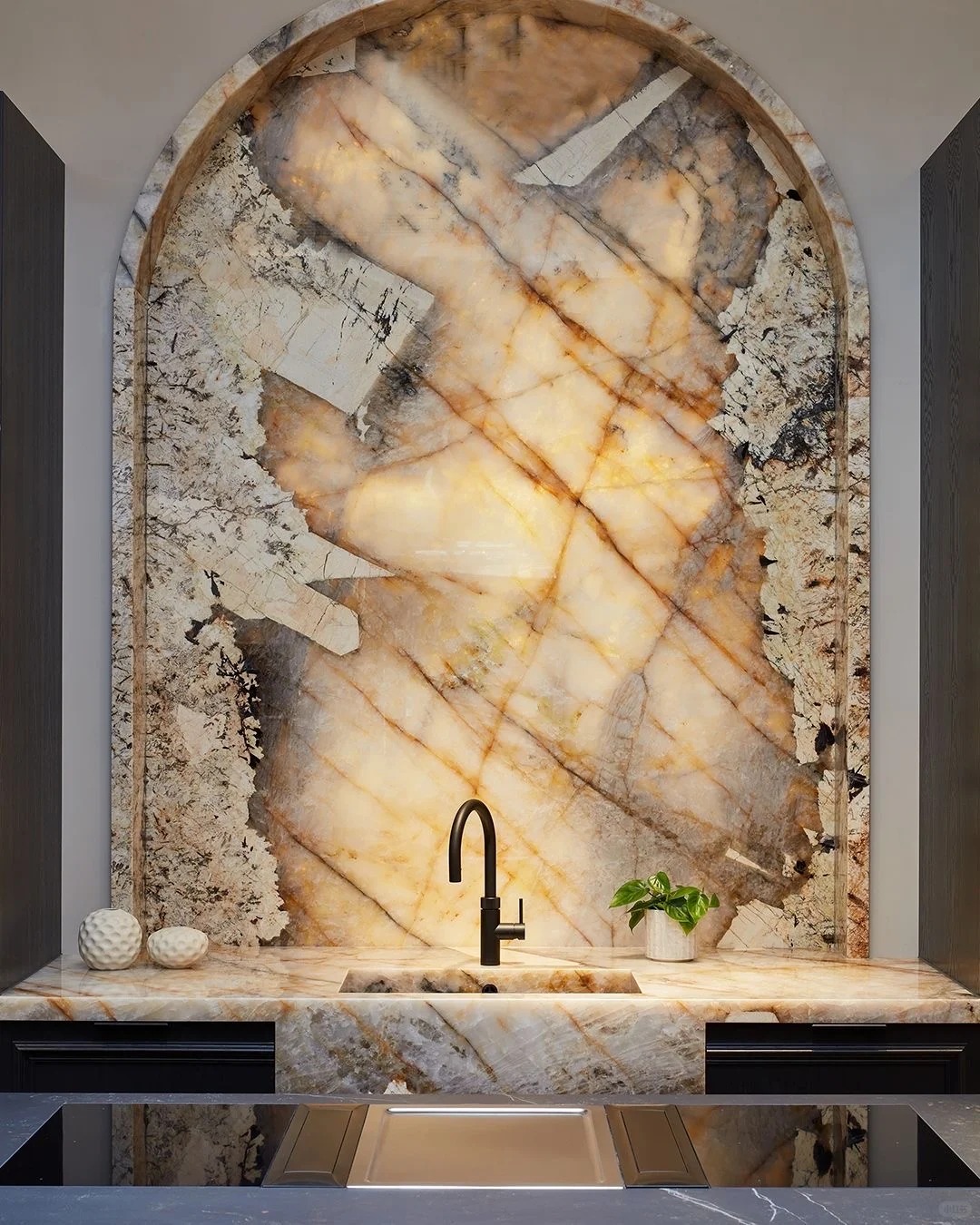 Backlit arched Patagonia stone backsplash above a dark vanity