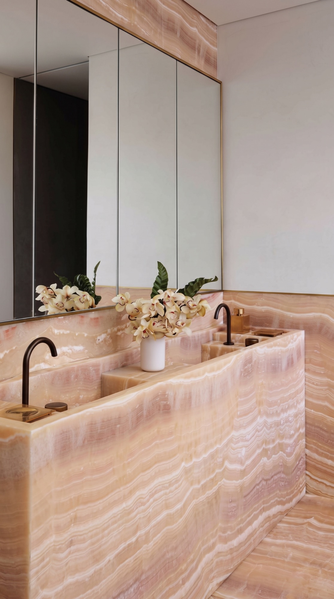 Backlit pink onyx double vanity with integrated stone basins in a warm contemporary bathroom