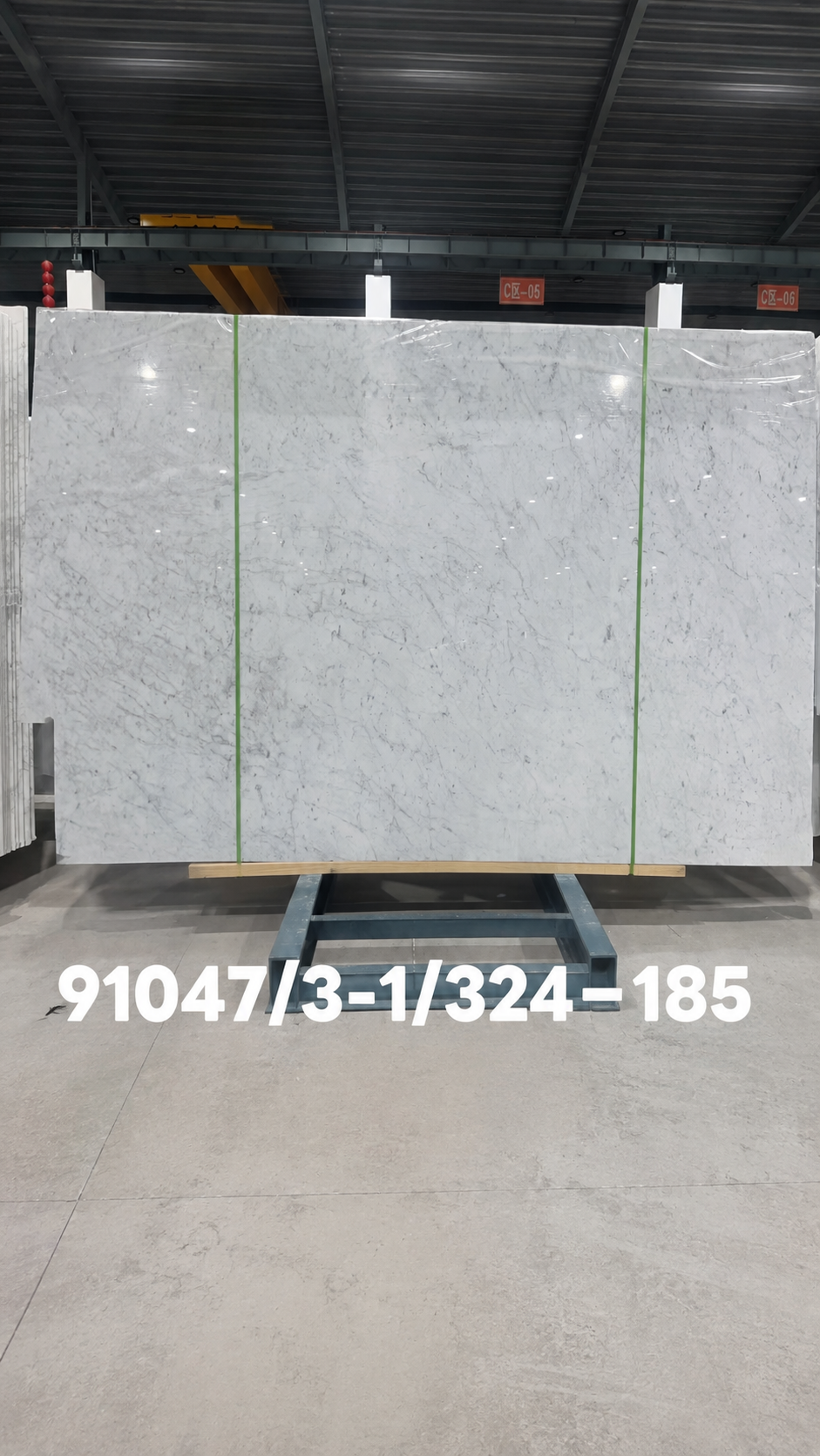 Carrara marble full slab with a white background and fine grey veining displayed in a stone warehouse