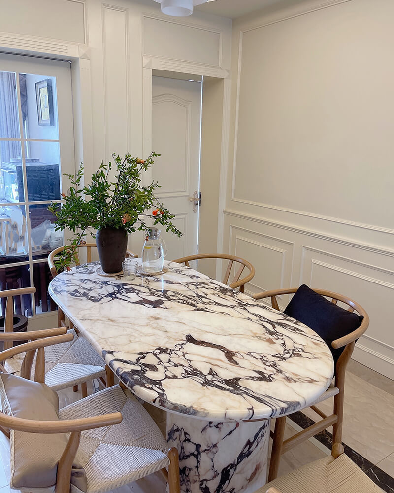 Oval Calacatta Viola marble dining table with cylindrical stone legs in a warm dining room